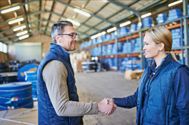 Shot of two people learning how to buy wholesale, shaking hands while working in a warehouse.